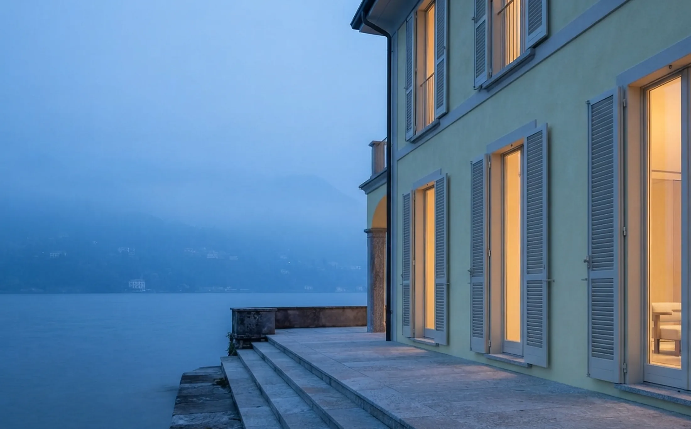 Lakeside villa at dusk with shuttered windows and stone terrace